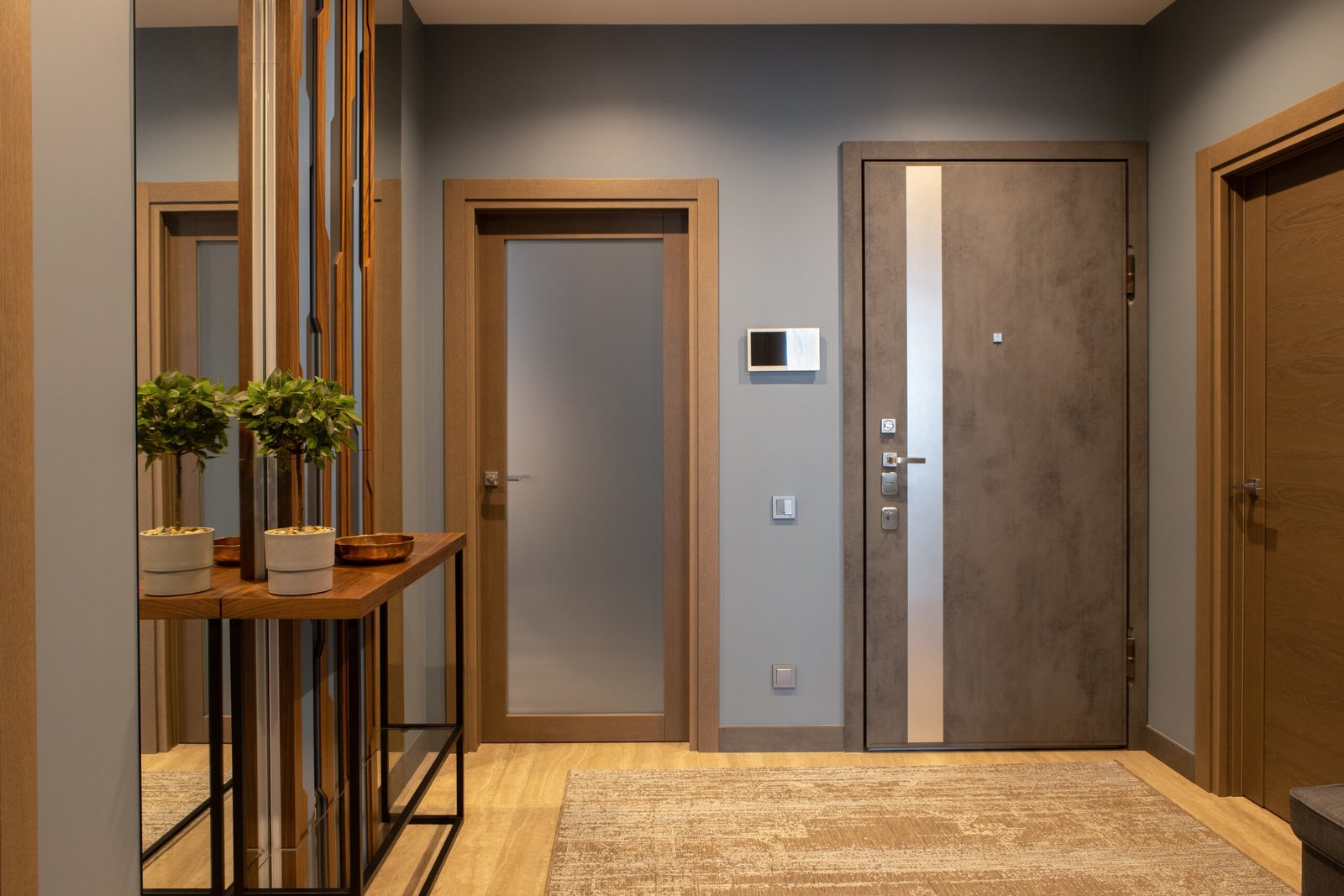 Modern entrance hallway in neutral shades of brown and gray tones in loft style. Video intercom on wall. Plant on console. Concept fashionable interior design, use of natural materials, technology.